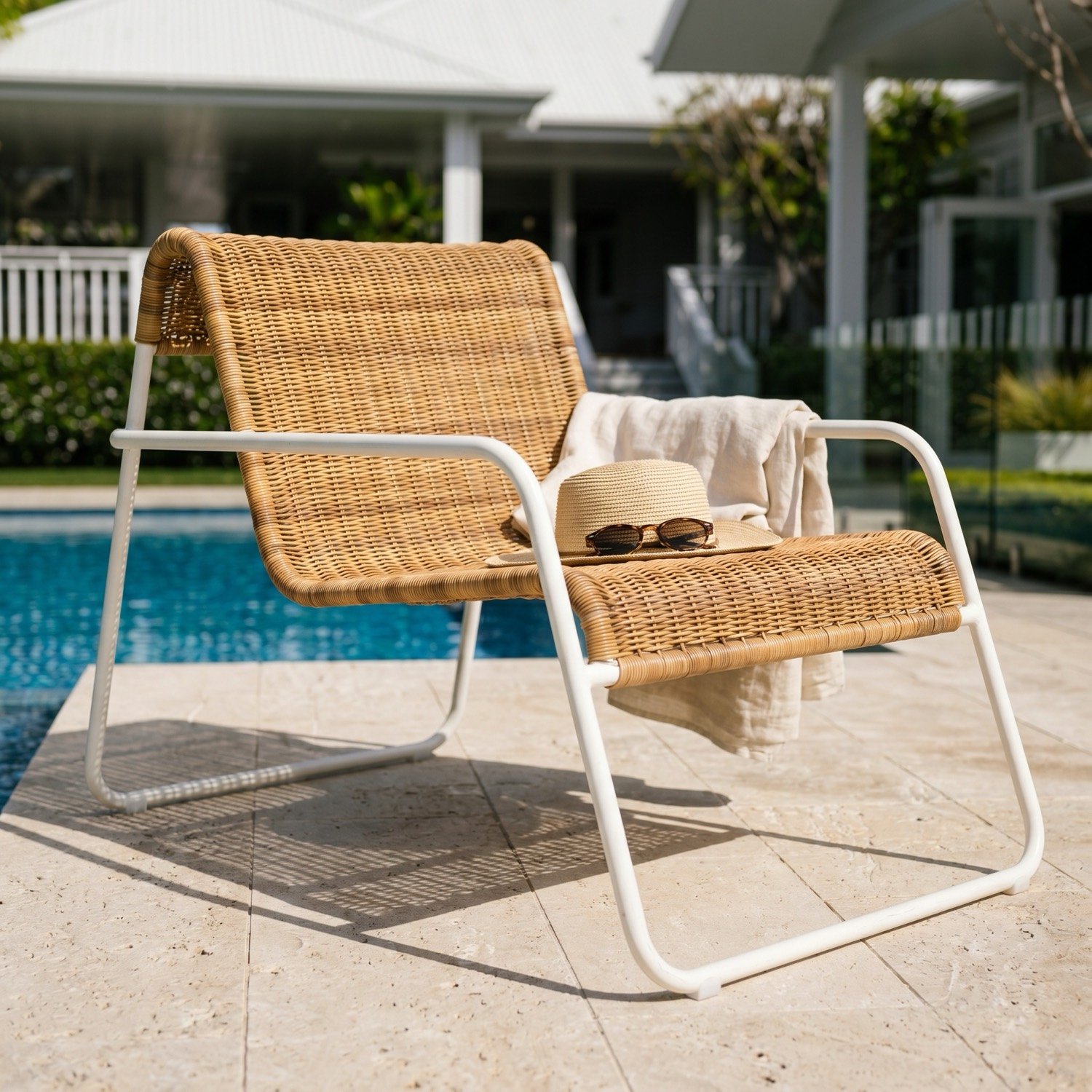 Woven lounge chair poolside with a hat and linen throw